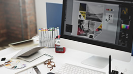 A Mac computer is shown with graphic design supplies on top of a desk