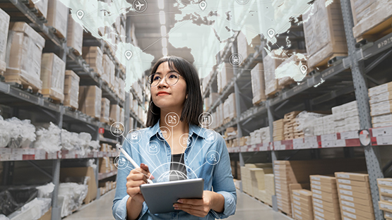 A woman with a tablet  examining the supplies in a warehouse.
